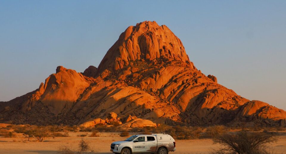 Dramatischer Sonnenuntergang über dem Spitzkoppe in Namibia mit Auto im Vordergrund