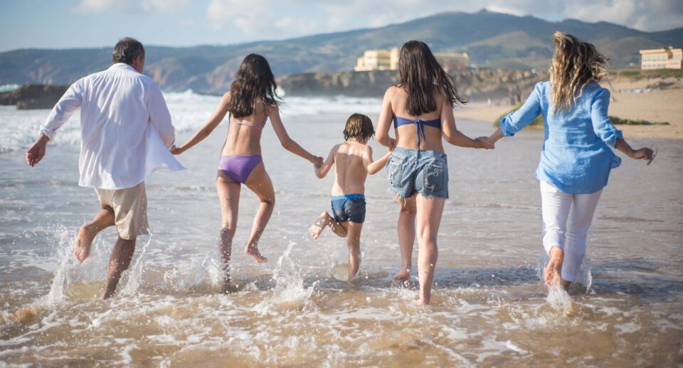 Familie rennt freudig in die Wellen am Strand Portugals an einem sonnigen Tag