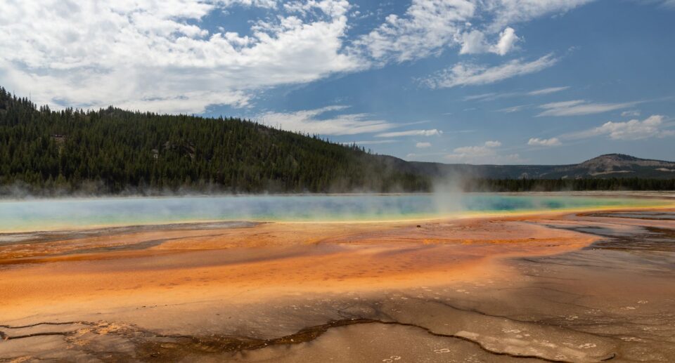 Farbenfrohe heiße Quelle im Yellowstone mit leuchtenden Mineralschichten unter blauem Himmel